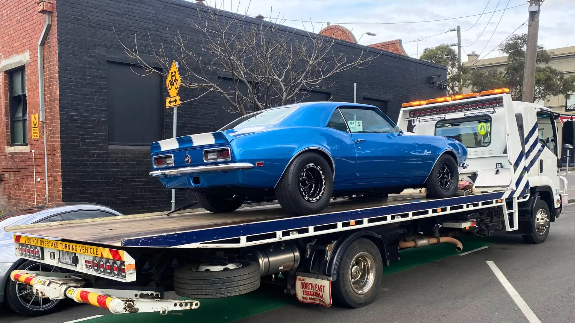 Blue Chevrolet Camaro SS on the All Over Towing tilt tray outside a Melbourne panel shop